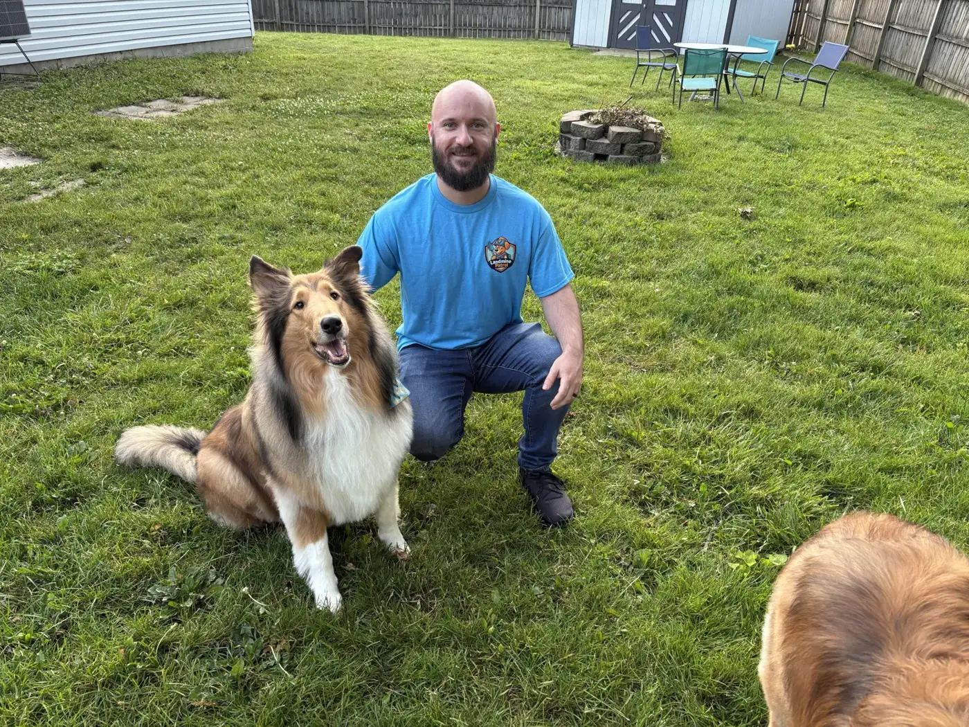 Landmine Patrol scooper kneeling with a happy collie in a clean backyard
