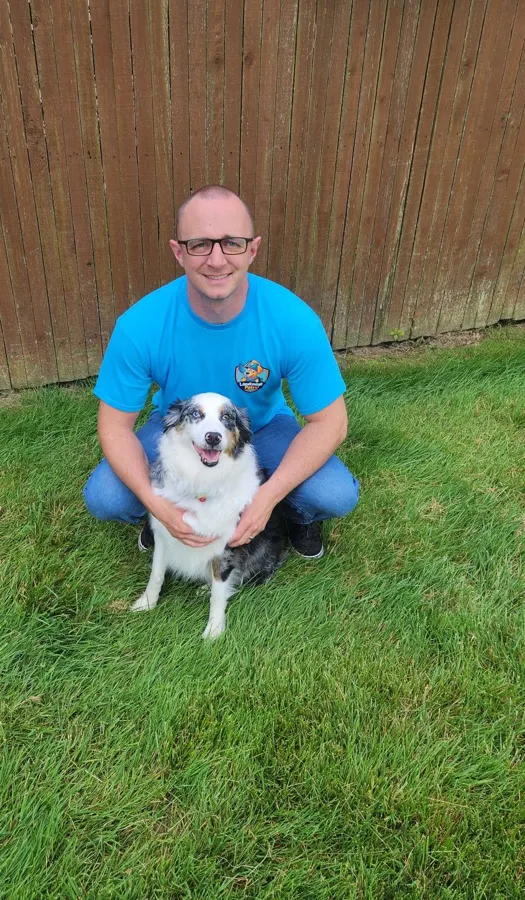 Landmine Patrol team member kneeling with an Australian shepherd